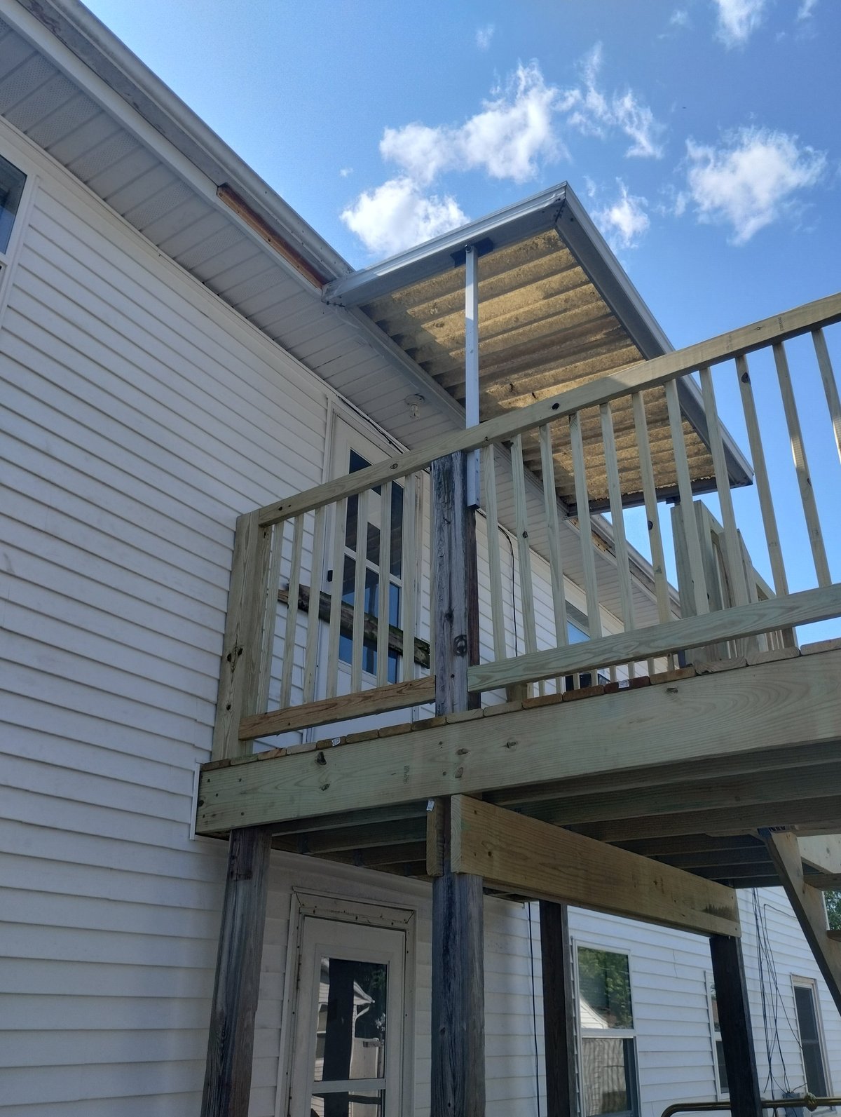 Two-story house with a newly framed wooden deck and railing in bright daylight