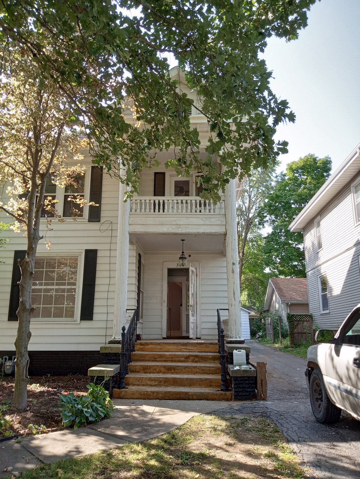 White two-story colonial-style house with red front door, restored balcony, and ivy-covered tree